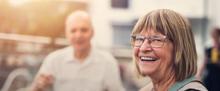 elderly woman smiling at café blurred man in background