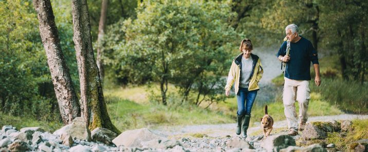 man and woman walking dog in forest