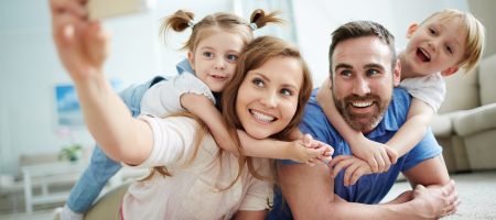 parents taking selfie with two young children on floor