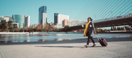 woman holding cup carying suitcase outside