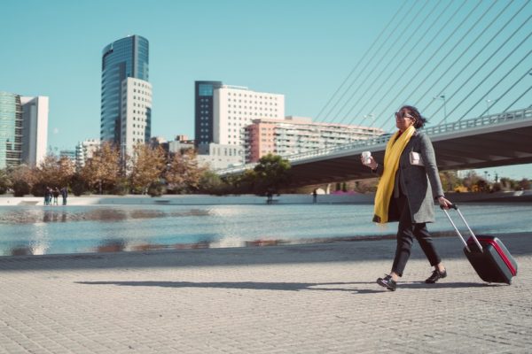 woman holding cup carying suitcase outside