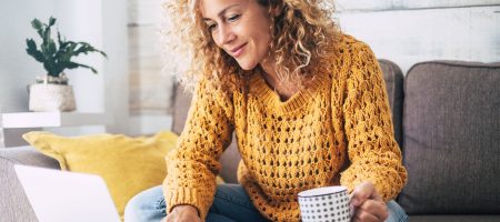 woman sitting on sofa using macbook holding mug